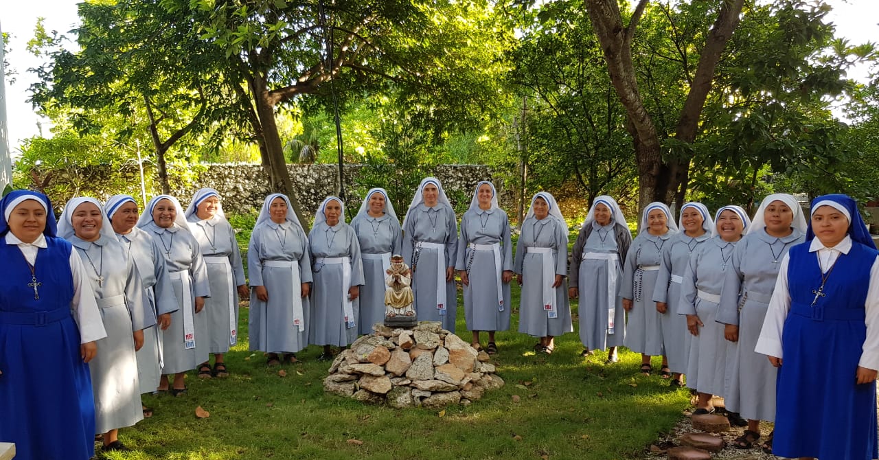 Comunidad de hermanas en el jardín alrededor de una imagen de la Virgen